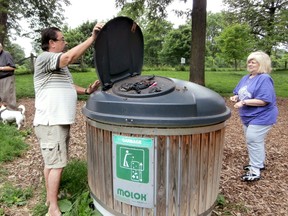 George Moogk and Susan Faist wrinkle their noses as they open the overflowing molok at the Greenway Off-Leash Dog Park in London. (AZZURA LALANI, The London Free Press)