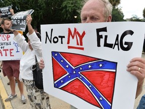A man holds a sign up during a protest rally against the Confederate flag in Columbia, South Carolina on June 20, 2015. The racially divisive Confederate battle flag flew at full-mast despite others flying at half-staff in South Carolina after the killing of nine black people in an historic African-American church in Charleston on June 17. Dylann Roof, the 21-year-old white male suspected of carrying out the Emanuel African Episcopal Methodist Church bloodbath, was one of many southern Americans who identified with the 13-star saltire in red, white and blue. AFP PHOTO/MLADEN ANTONOV