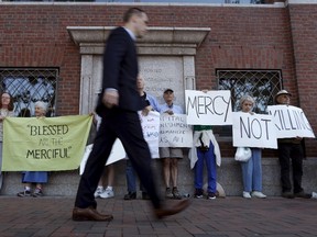 A pedestrian walks past death penalty protesters before the formal sentencing of convicted Boston Marathon bomber Dzhokhar Tsarnaev at the federal courthouse in Boston, Mass., on June 24, 2015. (REUTERS/Dominick Reuter)