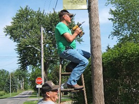 Fingal residents Ray Lunn, left, and Norm Clarke are seen installing utility pole banners that celebrate Fingal's proud history.