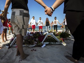 People hold hands as they pray in a circle around bouquets of flowers laid in tribute on the beach of the Imperial Marhaba resort, which was attacked by a gunman, in Sousse, Tunisia, June 28, 2015. (ZOHRA BENSEMRA/Reuters)