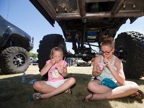 Chianne Manegre, 9, and her sister Alli Manegre, 13, eat ice drinks in the shade under a 1978 F250 Ford Ranger during the 31st Edmonton Summer Cruise Car Show, put on by the Edmonton Street Rod Association, in Sir Wilfrid Laurier Park on Saturday. David Bloom/Edmonton Sun/Postmedia Network