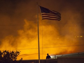 A U.S. flag is seen as a commercial building burns after being ignited by the Sleepy Hollow fire in Wenatchee, Washington June 29, 2015.  Emergency officials ordered hundreds of people to leave their homes in central Washington state as a fast-moving wildfire destroyed at least nine properties and threatened businesses on Sunday. Many took refuge in shelters as the blaze ripped across 1,700 acres near the cities of Cashmere and Wenatchee in Chelan County, about 120 miles (200km) east of Seattle.  REUTERS/David Ryder
