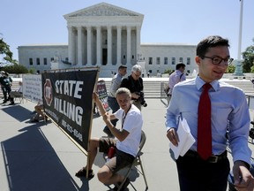 A news assistant runs past anti-death penalty demonstrators in front of the U.S. Supreme Court building in Washington on June 29, 2015. (REUTERS/Jonathan Ernst)