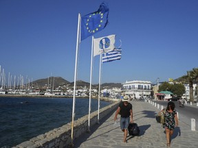 Tourists make their way past a European Union flag and a Greek national flag at the seaside of the island of Paros, Greece June 26, 2015. (REUTERS/Matthias Williams)
