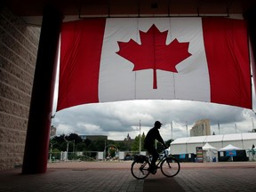 A man drive his bike past a Canadian flag at Ottawa City Hall. Tony Caldwell/Ottawa Sun files