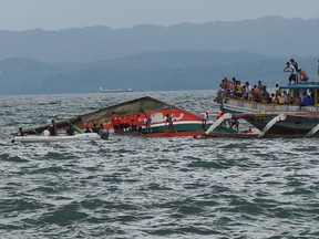 Rescuers help passengers from a capsized ferry boat, center, in Ormoc city on Leyte Island, Philippines, Thursday, July 2, 2015. A ferry capsized Thursday as it left a central Philippine port in choppy waters, leaving dozens dead and many others missing, coast guard officials said. (Ignatius Martin/Miquicar Photostudio via AP)