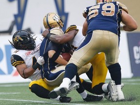 Tiger-Cats' Taylor Reed (left) and Adrian Tracy (second right) sack Blue Bombers quarterback Drew Willy (second left) during which he sustained an injury in CFL action in Winnipeg on Thursday, July 2, 2015. (John Woods/THE CANADIAN PRESS)