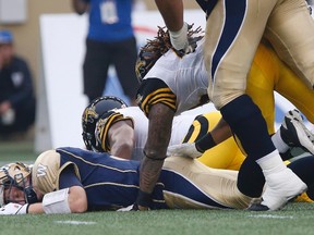 Winnipeg Blue Bombers' quarterback Drew Willy (5) lies unconscious after being sacked by Hamilton Tiger-Cats' Taylor Reed (44) and Adrian Tracy (93) during which he sustained an injury and was taken off during the first half of CFL action in Winnipeg Thursday, July 2, 2015. THE CANADIAN PRESS/John Woods