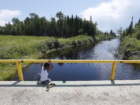 A boy from the Shoal Lake 40 First Nation sits on a bridge over a channel last month. (THE CANADIAN PRESS/John Woods file photo)