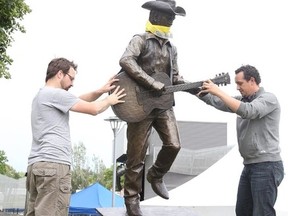 Gino Donato/The Sudbury Star
Tyler Fauvelle and Corey Lair, operations manager of Equipment World, place the bronze sculpture of Stompin' Tom Connors in Bell Park on July 3.