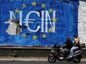 People ride past graffiti in Athens, Greece July 12, 2015. Euro zone leaders will fight to the finish to keep near-bankrupt Greece in the euro zone on Sunday after the European Union's chairman cancelled a planned summit of all 28 EU leaders that would have been needed in case of a "Grexit". REUTERS/Cathal McNaughton