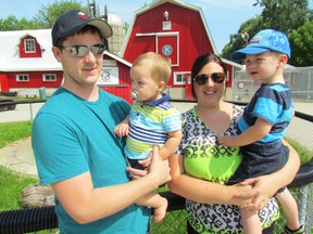 Geoff McKerracher, left, holds Carter McKerracher, 1, and his fiancee, Chloe Dennis, holds Cameron McKerracher, 2, at the Children's Animal Farm on Friday July 10, 2015 in Sarnia, Ont. The family organized an online auction that raised $3,250 for the farm located in Canatara Park.  (Paul Morden/Sarnia Observer/Postmedia Network)