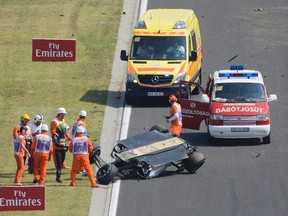 Force India driver Sergio Perez of Mexico (green helmet) stands next to his overturned car during the first practice session for the Hungarian Grand Prix on the Hungaroring circuit in Mogyorod, Hungary, on Friday, July 24, 2015. (Zsolt Czegledi/MTI via AP)