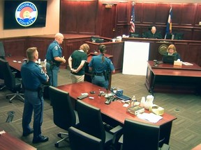 In this image made from Colorado Judicial Department video, Deborah Cave, center, in handcuffs and in the custody of sheriff's deputies, appears before Judge Carlos A. Samour Jr., top second from right, who sentenced her to three weeks in jail for contempt of court for earlier climbing over seats and shouting during the closing argument of the prosecution in the James Holmes trial's sentencing phase in Centennial, Colo., Thursday, July 30, 2015. Prosecutors are seeking the death penalty for Holmes, and jurors will decide at this stage whether to continue with the sentencing phase of the trial or to conclude by sentencing him to life in prison. (Colorado Judicial Department via AP, Pool)