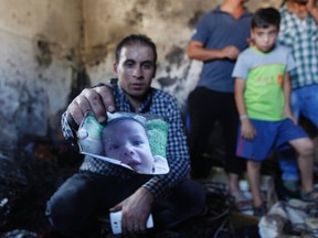 A relative holds up a photo of a one-and-a-half-year-old boy, Ali Dawabsheh, in a house that had been torched in a suspected attack by Jewish settlers in Duma village near the West Bank city of Nablus, on July 31, 2015. (AP Photo/Majdi Mohammed)
