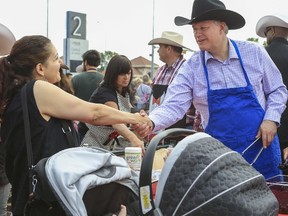 Prime Minister Stephen Harper, right, shakes hands with a woman while serving pancakes during the Calgary Stampede in Calgary, Alta., in this file photo taken July 4, 2015. (REUTERS/Crystal Schick/Files)