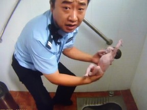 This frame grab of a police video taken on August 2, 2015 shows a policeman holding an abandoned newborn baby in a public toilet in Beijing. A newborn baby girl was abandoned in a Beijing public toilet and fell head-first down the pipe, reports said August 3, after her mother apparently gave birth in the facility.  CHINA OUT    AFP PHOTO