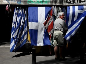 A man stands next to Greek national flag at a kiosk in central Athens, Greece, July 20, 2015. (REUTERS/Yiannis Kourtoglou)