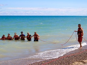 Sarnia firefighters link arms as they begin to scour the shore of Canatara Beach for a submerged dummy made of fire hose. The Wednesday morning exercise was the first training initiative this year in a series of collaborations between local firefighters and lifeguards to improve communications during a rescue operation. (Chris O'Gorman/The Observer/Postmedia Network)