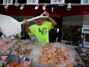 Juan Lara shovels ice onto fresh seafood at Captain White's Seafood City at The Wharf along the Washington Cannel in Washington, Thursday, July 30, 2015. (AP Photo/Carolyn Kaster)