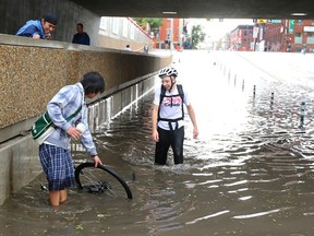 Ryan Drake (R) looks at his found bike in a flooded out 5 St. S.W. near 9 Ave in Calgary, Alta during another storm on Wednesday August 5, 2015. Drake has launched a campaign to find the Good Samaritan who helped out. Jim Wells/Calgary Sun/Postmedia Network