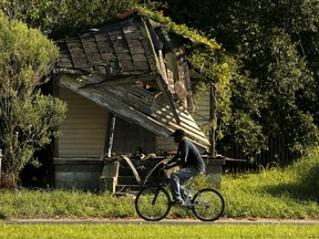 A man bikes past an abandoned house in the Lower Ninth Ward neighborhood of New Orleans, Louisiana, August 1, 2015. A decade after Hurricane Katrina, New Orleans seems to have found its rhythm again: the French Quarter is choked with tourists, construction cranes tower over the skyline, and hipsters bike to cafes in gentrifying neighborhoods.   REUTERS/Jonathan Bachman