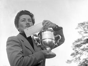 In this March 15, 1959 file photo, Louise Suggs of Atlanta, Ga., holds up the winner's cup and a check for $1,000 after winning the Women's Titleholders golf championship in Augusta, Ga.  (AP Photo/Horace Cort, File)