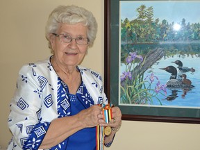 Helen McGuire holds an Ambassador for Peace medal awarded to her late husband John "Morley" McGuire at a ceremony in Burlington last month. The two were married for over 50 years until he died in 2007. The painting behind her is a paint-by-numbers project that Morley worked on which still hangs in Helen's bedroom. (Brent Boles, Postmedia Network)