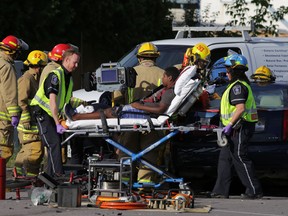 Frontenac County paramedics take an injured person to an ambulance as Kingston firefighters work to free another person from a car involved in a three-vehicle collision in Kingston, Ont. on Thursday, Aug 13, 2015. (Elliot Ferguson/The Whig-Standard)