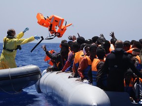A Belgian navy sailor passes life vests to migrants sitting in a rubber boat as they approach the Belgian Navy Vessel Godetia during a search and rescue mission in the Mediterranean Eea off the Libyan coasts, Italy, Tuesday, June 23, 2015. Hundreds of migrants were rescued on Tuesday by the Godetia, which is among a EU Navy vessels fleet taking part in the Triton migrants rescue operations. (AP Photo/Gregorio Borgia)