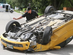 A Winnipeg Police officer examines a car that rolled at the intersection of Lodge Avenue and Conway Street in Winnipeg, Man. Sunday, Aug. 16, 2015. (Brian Donogh/Winnipeg Sun/Postmedia Network)