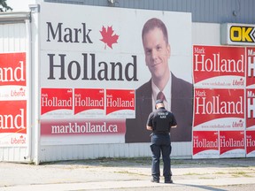 An officer with Town of Ajax bylaw services looks at campaign signs for federal Liberal Candidate Mark Holland at the corner of Kingston Rd. and Church St. in Ajax Monday August 17, 2015. (Ernest Doroszuk/Toronto Sun)