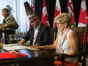 Ontario Regional Chief Isadore Day (centre) sits with Ontario Premier Kathleen Wynne (right) as Elder Garry Sault offers a prayer after they signed an accord at the Ontario Legislature in Toronto on Monday, August 24 2015. THE CANADIAN PRESS/Chris Young