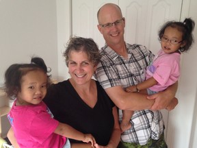 Johanne and Michael Wagner hold their twin girls, Binh, left, and Phuoc at their home in Kingston on Tuesday. Months after they both received life-saving liver transplants, the girls are improving dramatically. (Elliot Ferguson/The Whig-Standard)