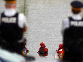 Mounties watch as members of Grande Prairie Technical Search and Rescue work in a large storm pond at 114 Street and 104 Avenue on Tuesday August 25, 2015 in Grande Prairie, Alta. TSR is assisting in an RCMP investigation relating to the murder of John Rick, who as shot dead outside the Canadian Brewhouse pub in Grande Prairie on October of 2014. Tom Bateman/Grande Prairie Daily Herald-Tribune/Postmedia Network