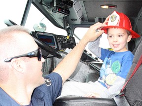 Firefighter Trevor Henri adjusts a helmet for four-and-a-half-year-old Dean Clarke at New Sudbury Days on Saturday. Ben Leeson/The Sudbury Star/Postmedia Network