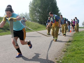 Some of the Rustlers’ players watch as one of the girls try the tire pull with in full firefighting attire during the warm, humid day.