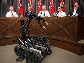A new Winnipeg Police bomb robot sits at a press conference on proceeds of crime in front of (from left) Jack Harrigan, RCMP Assistant Commissioner Kevin Brousseau, Attorney General Gord Mackintosh, Winnipeg Police deputy chief Danny Smyth and Gord Schumacher. (Brian Donogh/Winnipeg Sun)