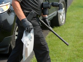 A London police forensic officer carries a gun out of a house on Briar Court after an alleged long-running neighbourhood dispute led to shots being fired. (Free Press file photo)