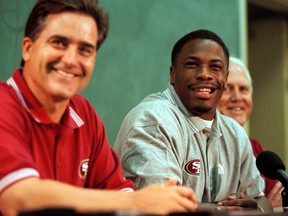 In this July 26, 1999, file photo, newly-signed San Francisco 49ers running back Lawrence Phillips, center, smiles with 49ers head coach Steve Mariucci, left, and general manager Bill Walsh during a news conference at training camp in Stockton, Calif. (AP Photo/Brian Baer, File)