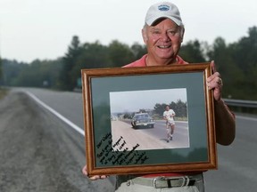 LUKE HENDRY/THE INTELLIGENCER
Walter Sawkins, standing on Highway 7 in Tweed, holds a photo of Terry Fox running on Highway 7 ahead of Sawkins' Ontario Provincial Police cruiser. Taken in 1980 by Tom Hinzke, the photo was later signed by Fox's sister, Judith.