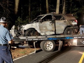 A police officer watches as a cruiser that was shot at is removed from Forest Road, Wednesday, Sept. 2, 2015 in Millis, Mass. Police are looking for a gunman who fired at a police cruiser in a town southwest of Boston, and schools are being closed as a precaution. (John Blanding/The Boston Globe via AP, Pool)