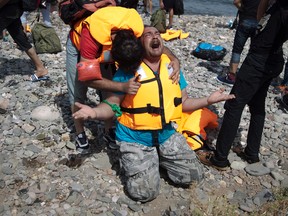 Syrian refugees react as they arrive after crossing aboard a dinghy from Turkey, on the island of Lesbos, Greece, Monday, Sept. 7, 2015. The island of some 100,000 residents has been transformed by the sudden new population of some 20,000 refugees and migrants, mostly from Syria, Iraq and Afghanistan. (AP Photo/Petros Giannakouris)