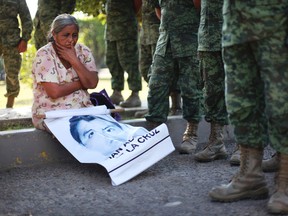 In this Dec. 18, 2014 file photo, the mother of missing college student Adan Abarajan de la Cruz sits at the foot of soldiers outside a military base during a protest by the families of 43 missing students. A group of independent experts said Monday, Aug. 17, 2015, that Mexican authorities withheld information from family members of students who disappeared after a confrontation with police. (AP Photo/Felix Marquez, File)