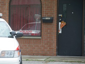 A police officer sits in a cruiser outside a social club where Steve Sinclair was fatally shot at 1161 Hamilton Rd. in London. A bouquet of flowers is wedged into the club door handle. (CRAIG GLOVER, The London Free Press)