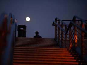 The moon is seen as a man walks on a pedestrian bridge in Shanghai December 4, 2014. REUTERS/Carlos Barria