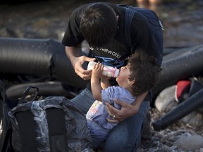 An Afghan refugee feeds a baby milk moments after arriving on the Greek island of Lesbos, September 9, 2015. Greece asked the European Union for aid to prevent it being overwhelmed by refugees, as a minister said arrivals on Lesbos had swollen to three times as many as the island could handle. (REUTERS/Dimitris Michalakis)