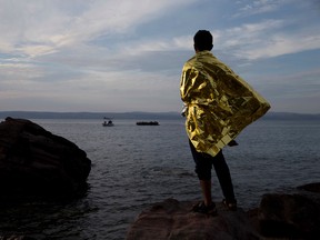A refugee wrapped in a thermal blanket  looks at a dinghy full of migrants and refugees approach the coast of Lesbos island, Greece, Wednesday, Sept. 9, 2015. The head of the European Union's executive says 22 of the member states should be forced to accept another 120,000 people in need of international protection who have come toward the continent at high risk through Greece, Italy and Hungary. (AP Photo/Petros Giannakouris)