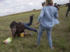 A migrant carrying a child falls after tripping on a Hungarian TV camerawoman, right, while trying to escape from a collection point in Roszke village, Hungary, September 8, 2015. (REUTERS/Marko Djurica)